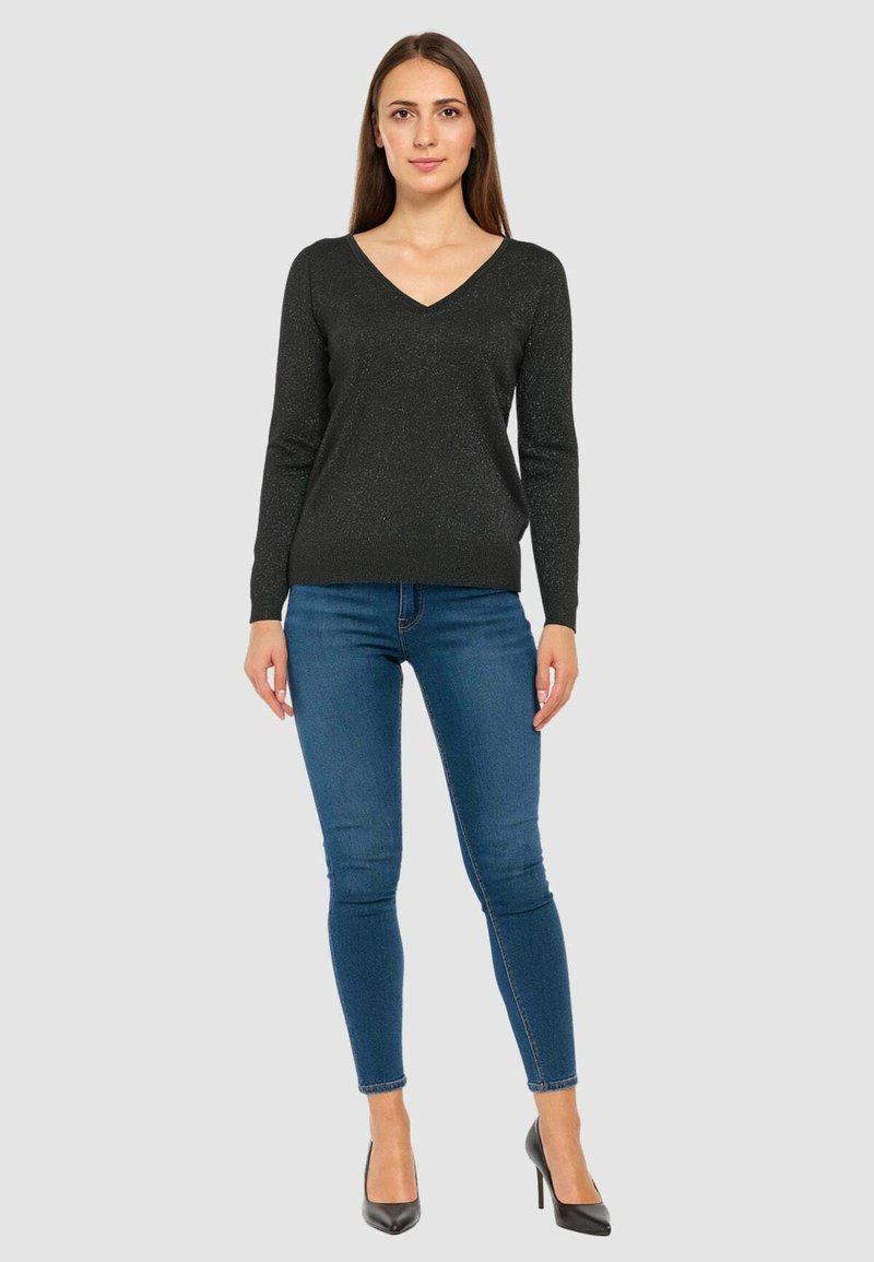Maglione nero aderente con scollo a V e maniche lunghe, realizzato in un materiale glitterato. Abbinato a jeans blu slim e tacchi alti neri.