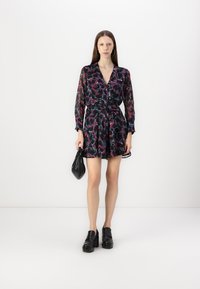 Robe noire à fleurs avec de longues manches en voile, un col et une taille cintrée. Assortie à des chaussures noires à plateforme épaisses et un petit sac à main noir.