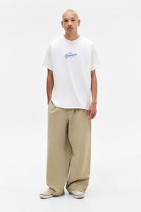 White cotton T-shirt with "FRESH Groceries" blue text, paired with loose beige trousers, and canvas shoes. Simple design, no patterns.