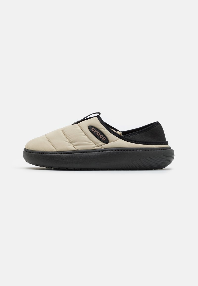 Beige slip-on sko med quiltat mönster, svarta accenter och sula av gummi. Har en liten logotyp på sidan och en strukturerad sula.