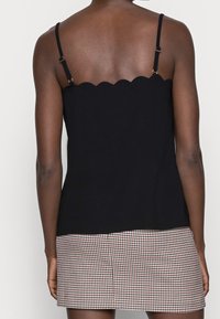Camisole en maille noire avec décolleté festonné, bretelles réglables et design uni ; associée à une jupe pied-de-poule rouge et blanche.