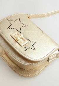 Guldmetal crossbody taske med stjerneudskæringer, en frontklap og en guldfarvet lås. Glat tekstur med en let glitrende overflade.