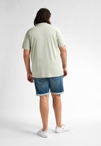 Ljust grönt kortärmat skjorta med en avslappnad passform, parat med blå denimshorts med uppvikt fåll och vita träningsskor.