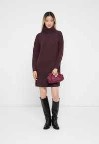 Burgundi miegamosios megztinis su ilgomis rankovėmis, suderintas su purpurine rankine ir juodais oda iki kelių batais.