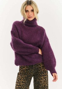 Fialový, nadmerne veľký rolákový sveter s rebrovanými manžetami. Mäkká textúra, balónové rukávy. Kombinovaný s nohavicami s leopardím vzorom.