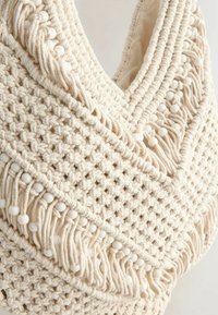 Macramé tas in crèmekleur, met ingewikkelde knopen, een gestructureerd oppervlak en witte kralenaccenten langs de randen.