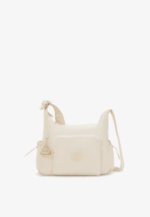 Helles beiges Schultertasche mit vorderer Reißverschlusstasche, Affen-Schlüsselanhänger und verstellbarem Tragegurt auf einem weißen Hintergrund.