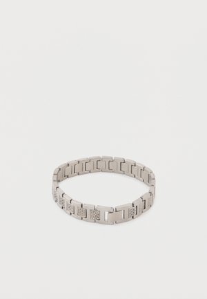 Bracelet à maillons en métal argenté avec des maillons rectangulaires alternant entre lisses et gravés, fermés en forme circulaire sur un fond blanc.