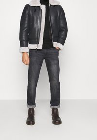 Pilotjacka i läder med en krämfärgad fårskinnskrage och muddar, kombinerad med mörka jeans och bruna läderstövletter. Minimalistisk design.