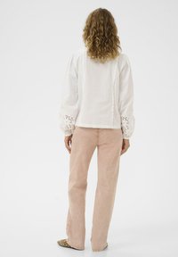 Blouse blanche avec manches texturées brodées et détails en feston. Associée à un pantalon rose clair et des chaussures à motifs.