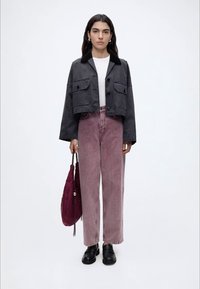 Femme portant une veste courte noire, une chemise blanche, un jean taille haute mauve, des mocassins noirs et tenant un sac à main bordeaux.
