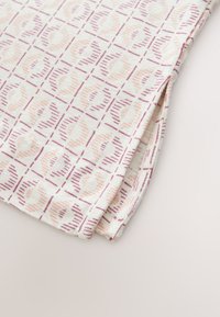 Pamut anyag ismétlődő mintával, amely puha rózsaszín és mályva köröket ábrázol strukturált vonalak körvonalazásával, a sarkánál összehajtva.