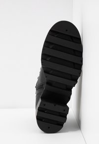 Suola di scarpa nera realizzata in un materiale di gomma testurizzato, con un design rigato e quattro distintivi punti circolari accentati.