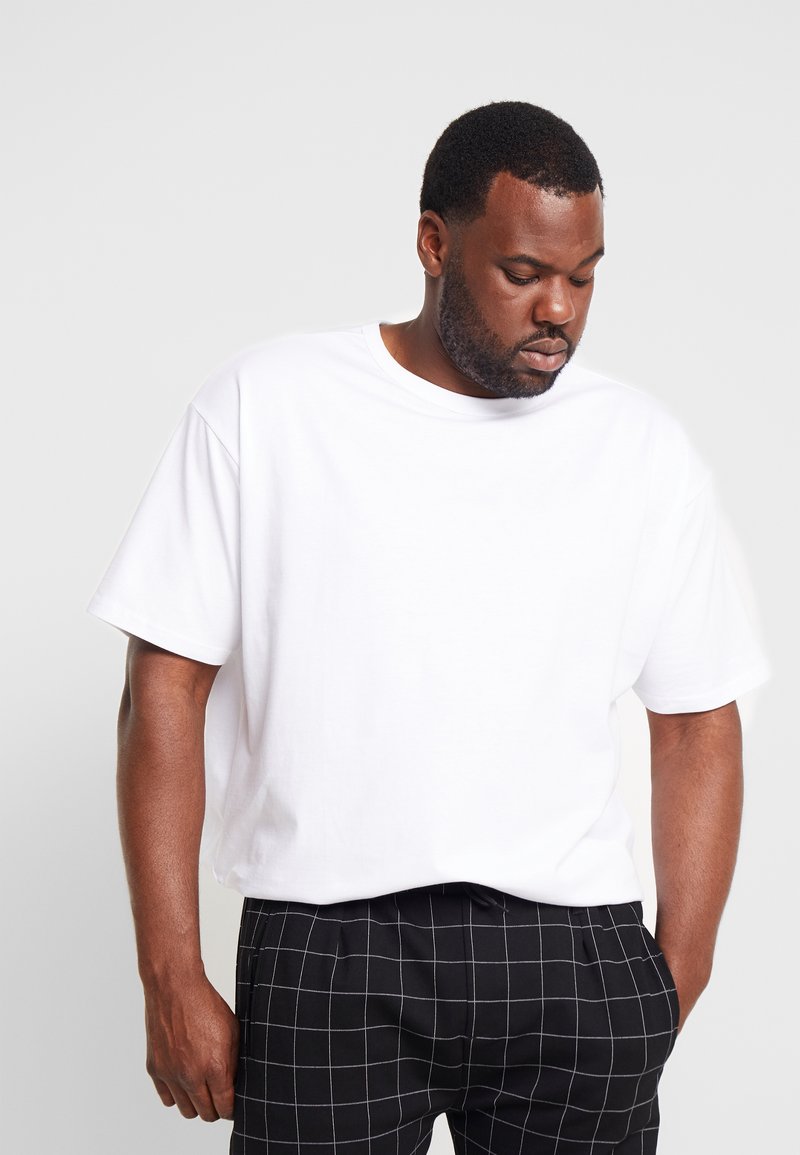 Witte katoenen t-shirt met een ontspannen fit en ronde hals, gecombineerd met zwarte geruite broeken met witte lijnen. Eenvoudig en veelzijdig ontwerp.