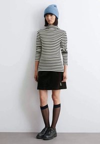 Maglione a collo alto a righe bianche e nere, abbinato a una gonna in cotone nero a coste, calze trasparenti nere fino al ginocchio e scarpe nere. Berretto azzurro chiaro.