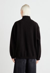 Schwarze Fleecejacke mit hohem Kragen, lockerer Passform und elastischen Bündchen. Strukturiert Oberfläche, kombiniert mit dunklen, lässig geschnittenen Hosen.