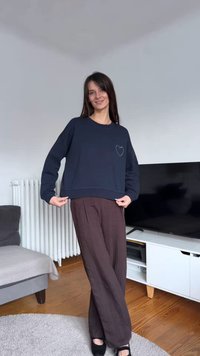 Sudadera corta azul marino con detalle de corazón de pedrería, combinada con pantalones marrones holgados, ambientada en una sala de estar.