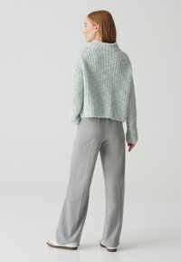 Maglione spesso a maglia verde chiaro con una texture a coste, abbinato a pantaloni a gamba larga grigio chiaro e sneakers bianche, visto da dietro.