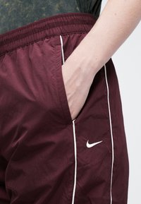 Bordo sporta šorti ar baltu sānu apdari un Nike logo. Iezīmējas ar elastīgu jostasvērpu un sānu kabatām. Strukturēts, viegls materiāls.