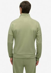 Sudadera atlética de color verde oliva con un cuello alto y puños acanalados, que presenta una textura suave y un corte holgado. Vista trasera.