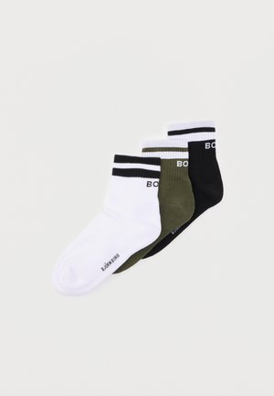 Trois paires de chaussettes basses en blanc, vert olive et noir, chacune avec deux bandes horizontales et le texte de la marque près du bord de la cheville.