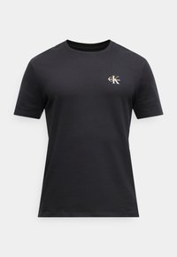 T-shirt noir à manches courtes avec col rond, orné d'un petit logo "CK" Calvin Klein blanc et doré sur le haut du côté gauche de la poitrine.