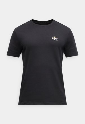 Svart T-skjorte med korte ermer og rund hals med liten hvit og gull Calvin Klein "CK"-logo på øvre venstre bryst.