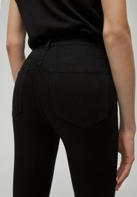 Black denim jeans with a fitted design, tactile texture, and back pockets. High-waisted with belt loops and clean stitching details.