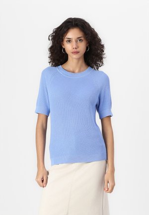 Pull en tricot côtelé bleu clair à manches courtes, col rond et coupe ajustée, porté avec une jupe beige, sur un fond blanc.