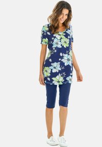 Navy bloemen tuniek met korte mouwen, voorzien van witte en groene bloemen, gecombineerd met knielange navy shorts en witte sneakers.