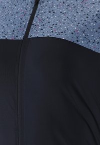 Veste légère avec une partie supérieure bleu moucheté et une partie inférieure noire unie. Elle possède une fermeture éclair centrale et une texture lisse.