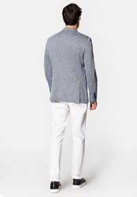 Marynarka w niebiesko-białą kratkę, z pojedynczym rozcięciem, zestawiona z białymi spodniami i ciemnymi sneakersami.