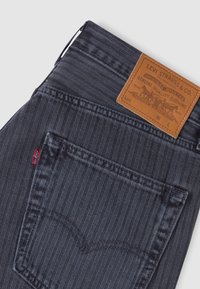 Τσεπάκι από σκούρο μπλε τζιν Levi's με σχέδιο ψαροκόκκαλο, κόκκινη ετικέτα Levi's και δερμάτινη καφέ ετικέτα της μάρκας Levi Strauss & Co. πάνω από αυτήν.