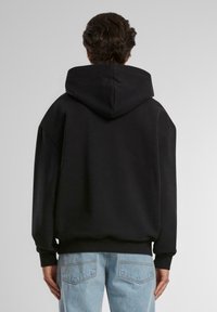 Sort hættetrøje med afslappet pasform, der har en stor hætte, ribbede manchetter og ensfarvet design. Sættes sammen med lyseblå jeans.