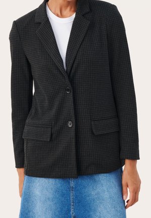 Blazer noir à carreaux avec revers cranté, deux poches avant et fermeture à un bouton. Porté sur un t-shirt blanc, la texture est subtile.