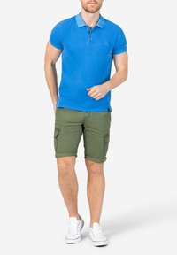 Blaues Baumwoll-Polohemd mit Kragen, kombiniert mit khakifarbenen Cargo-Shorts in Kniehöhe. Weiße Schnürsneaker runden das Outfit ab.