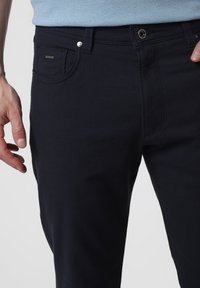 Jeans w kolorze granatowym, z fakturowanej tkaniny, z przednią kieszenią, metalowymi elementami i małym logo w pobliżu kieszeni. Dopasowany krój.