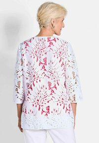 Weißes Spitzenoberteil mit rosa Blattmustern, Dreiviertelärmeln und einem offenen Rückendesign. Strukturierter, leichter Stoff mit Ausschnitten.