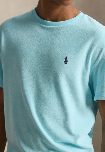 Άνδρας που φοράει ανοιχτό μπλε πουκάμισο με κοντά μανίκια και μικρό σκούρο κεντημένο λογότυπο με παίκτη πόλο στο στήθος.