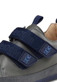Grauer Schuh mit marineblauen Riemen, der ein Bärenmotiv an den Riemenenden aufweist. Textiloberfläche und glattes Leder, abgerundete Zehenform.