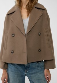 Brown double-breasted jacket made of soft fabric, featuring a wide collar, large buttons, and side seam pockets. Worn over a gray top.