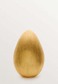 Huevo decorativo dorado con un acabado suave y mate, forma redondeada y líneas texturizadas sutiles, de pie contra un fondo claro.