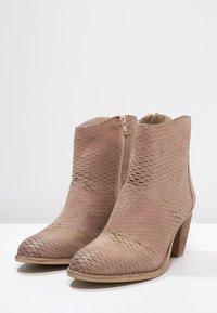 Light beige ankle boots made from perforated leather, featuring a side zipper and a stacked heel for a textured, fashionable look.