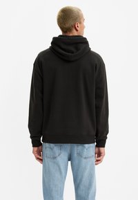 Sudadera negra con capucha, de textura suave, corte holgado y puños acanalados, combinada con jeans de color azul claro.