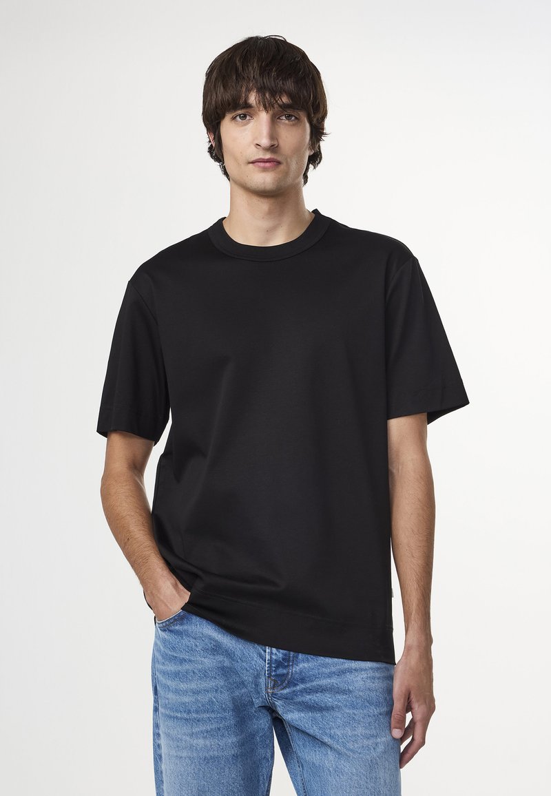 T-shirt en coton noir à col rond et manches courtes, avec une coupe décontractée et une texture douce, associé à un jean bleu clair.