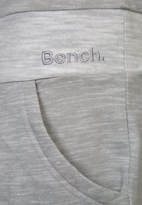 Szare dresowe spodnie z gładkiego materiału, z szerokim elastycznym paskiem w talii. Na pasku wyszyty jest napis "Bench." w pasującym odcieniu szarości.