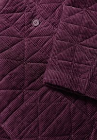 Tkanina z żebrowanego weluru w głębokim purpurowym kolorze, z diamentowym wzorem i detalem w postaci guzika. Miękka faktura z widocznym żebrowaniem.