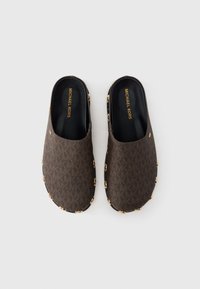 Καφέ παπούτσια τύπου κλόγκ με κλείσιμο χωρίς κορδόνια, με υφή στο πάνω μέρος που φέρει μοτίβο μονόγραμμα, διακοσμητικά στοιχεία σε χρυσό τόνο κατά μήκος των πλευρών και μαύρα εσωτερικά πέλματα.