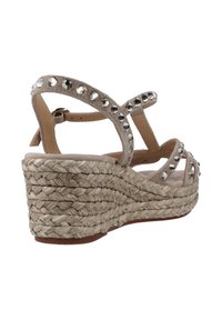 Sandali wedge beige con suola in juta intrecciata, caratterizzati da cinturini incrociati decorati con borchie argentate e una morbida texture in suede.