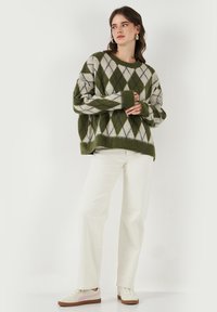 Roheline ja valge argyle-mustriga oversized-sviiter ribatud varrukatega, kantud valgete laia säärte teksade ja heledate sportkingadega, millel on tekstureeritud kudumine.